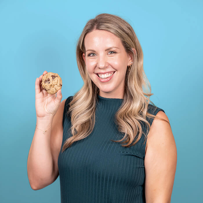 Headshot of a women in a blue top holding a cookie | Caitlyn Trainor