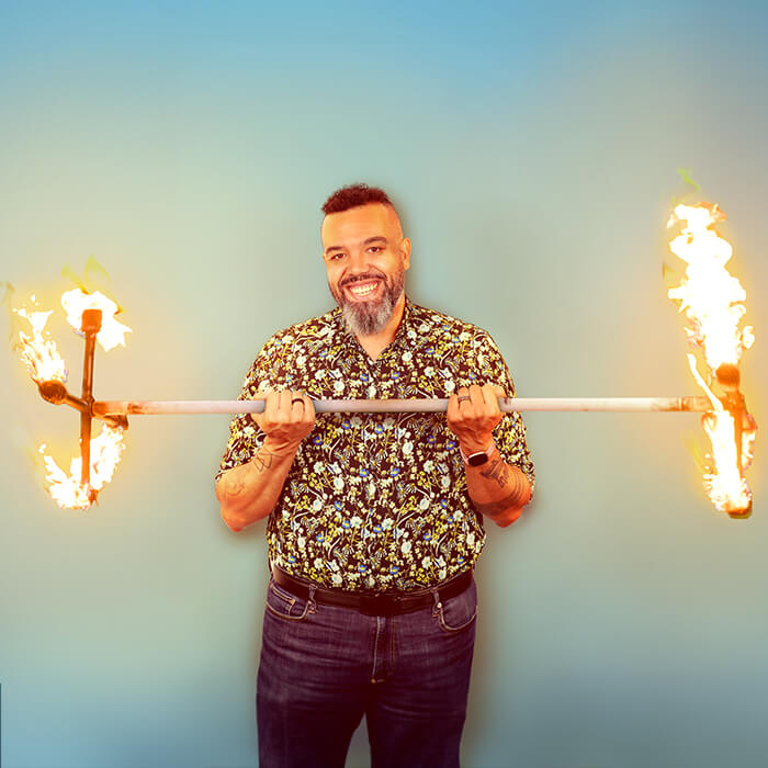 Headshot of a man in a floral shirt holding a bar on fire | Marcus Kent