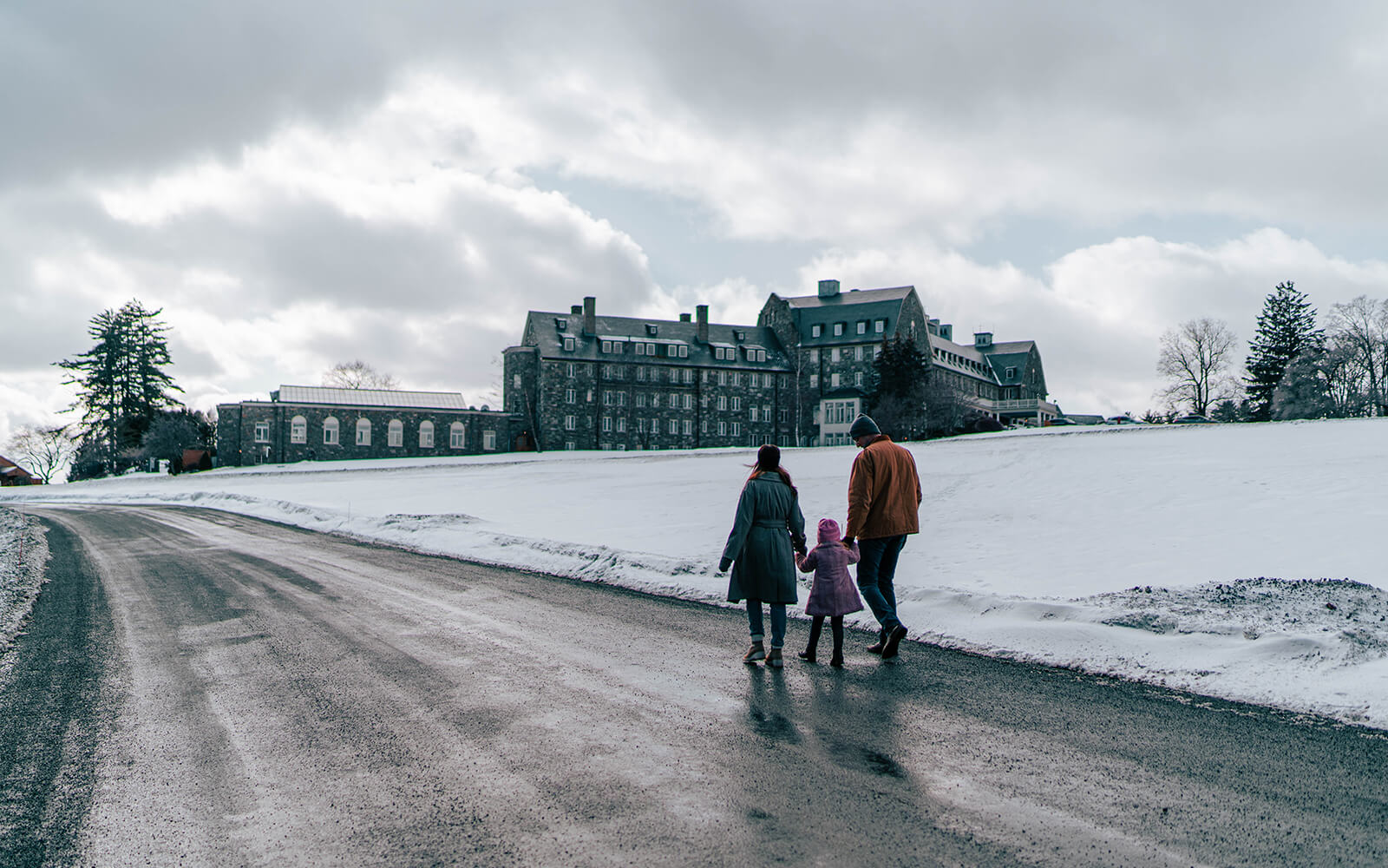 Two adults and a child walking outside Skytop Lodge in the Snow