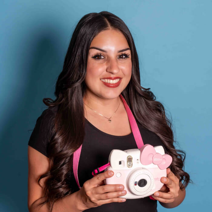 Headshot of a women in a black shirt holding a polaroid camera| Rochelle Perez