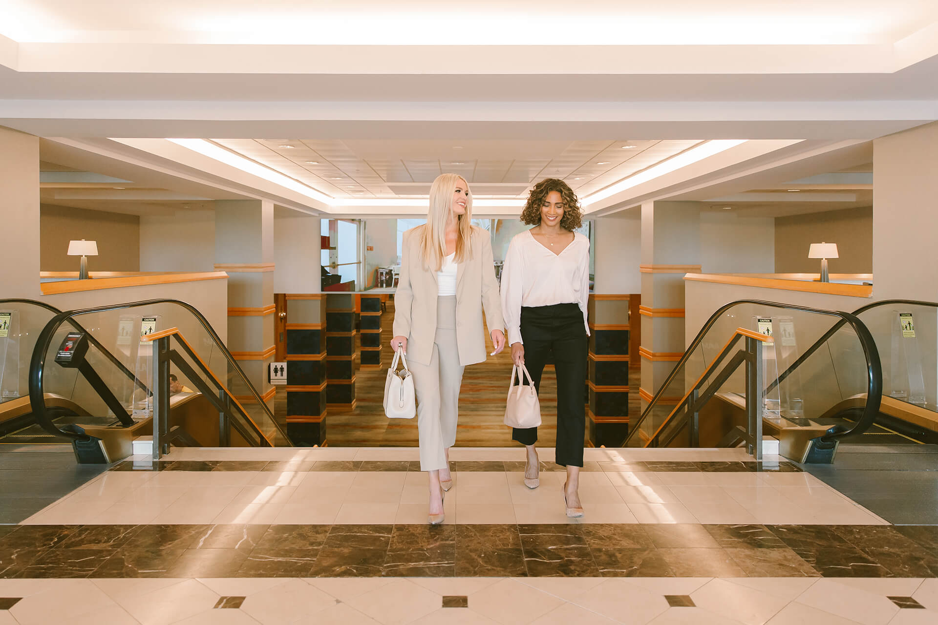 Two women walking inside by escalators