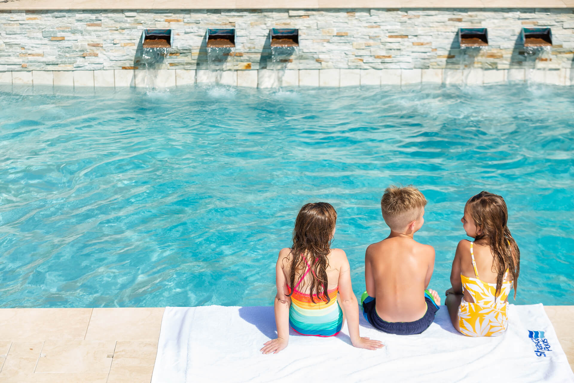 Three kids sitting by a pool