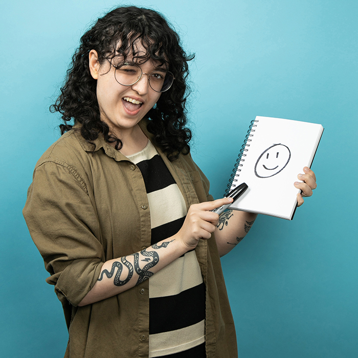 Headshot of a Women in a green shirt holding a picture of a smiley face drawing