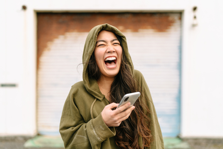 Portrait of young woman holding smart phone and laughing