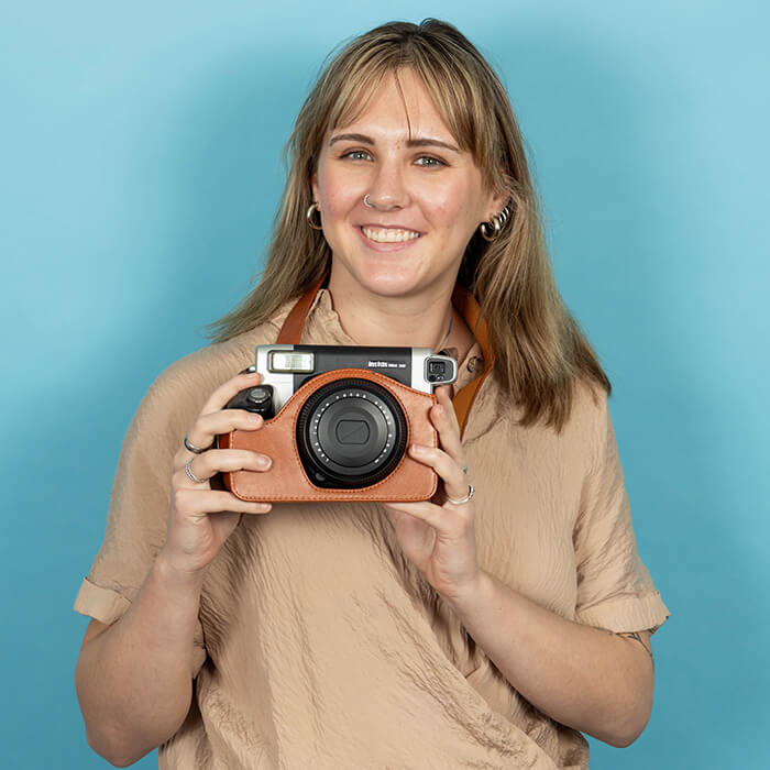 Headshot of a women in a tan top holding a camera